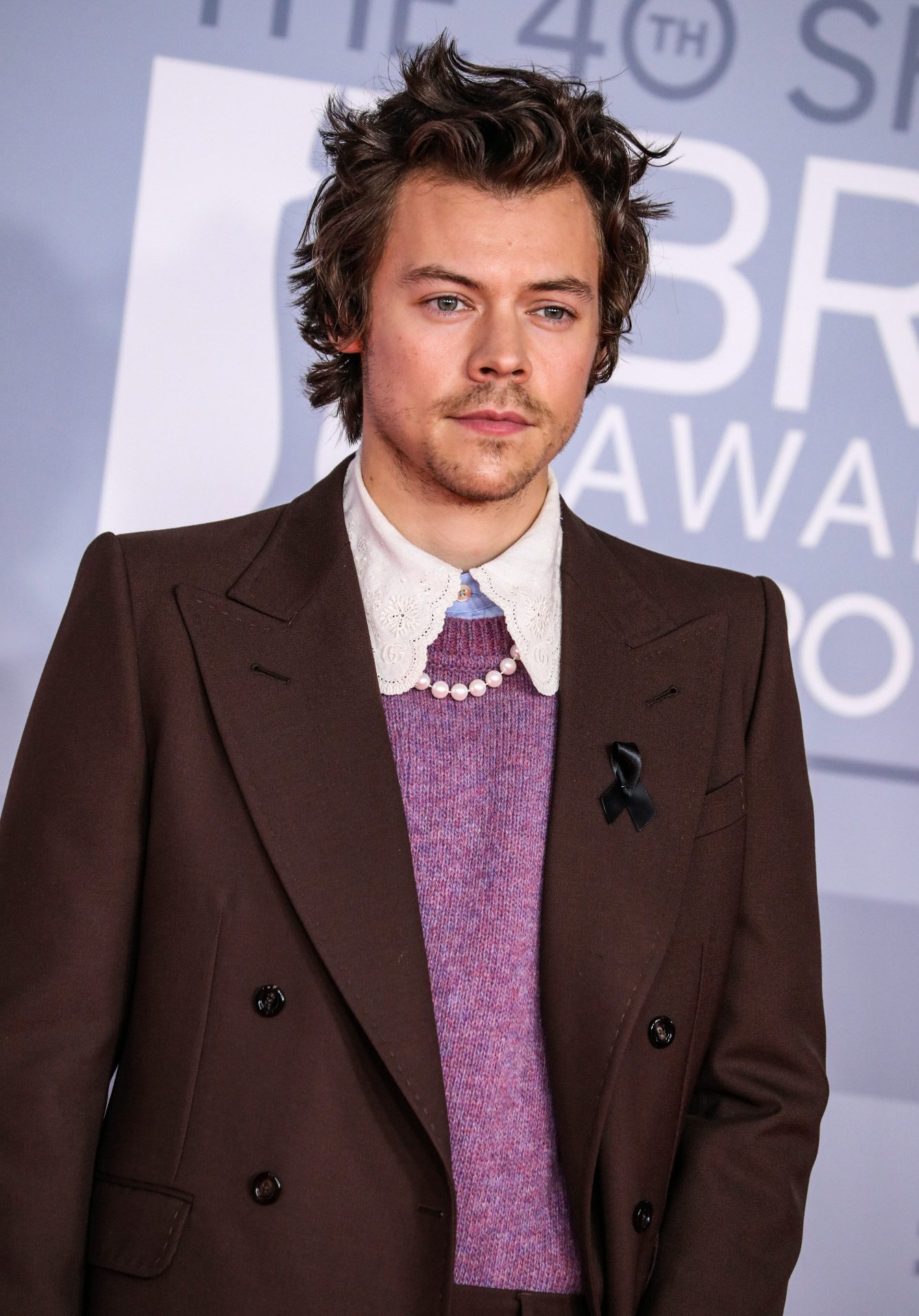 Harry Styles avec un collier de perles avec un de ses looks transgressifs.