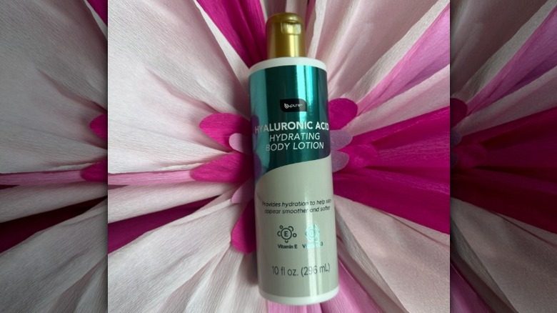 Une bouteille de lotion pour le corps hydratant de l'acide hyaluronique de B.Pure sur une toile de fond florale
