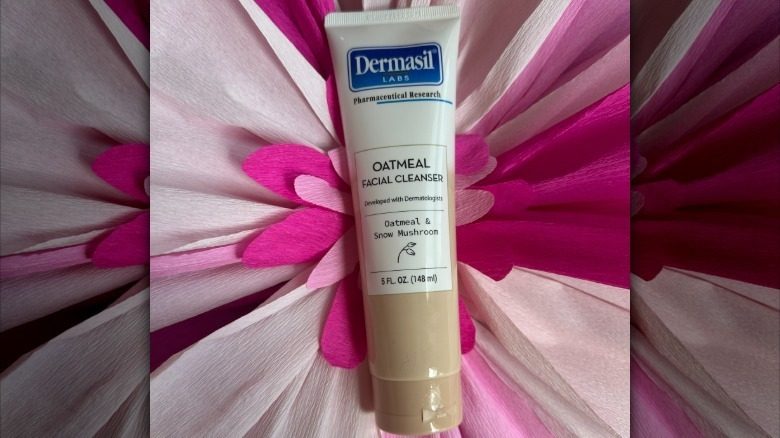 Une bouteille de nettoyant pour le visage à l'avoine de Dermasil Labs sur une toile de fond florale