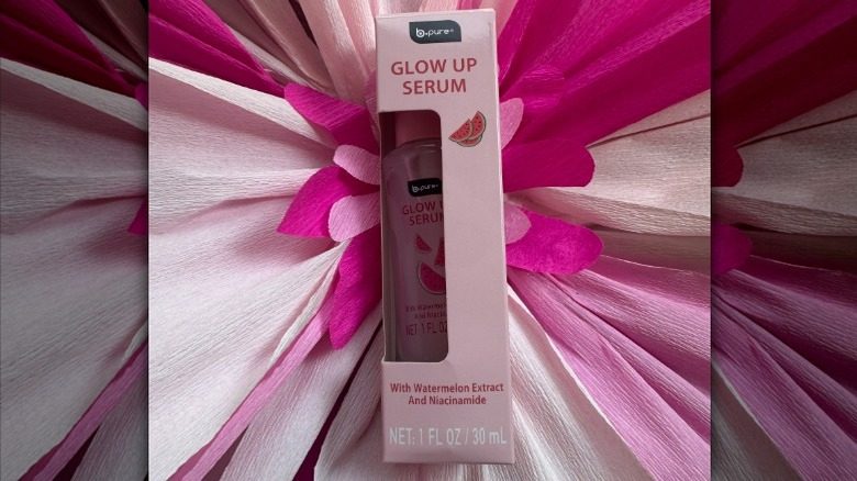 Une bouteille de sérum brillante de B.Pure sur une toile de fond florale