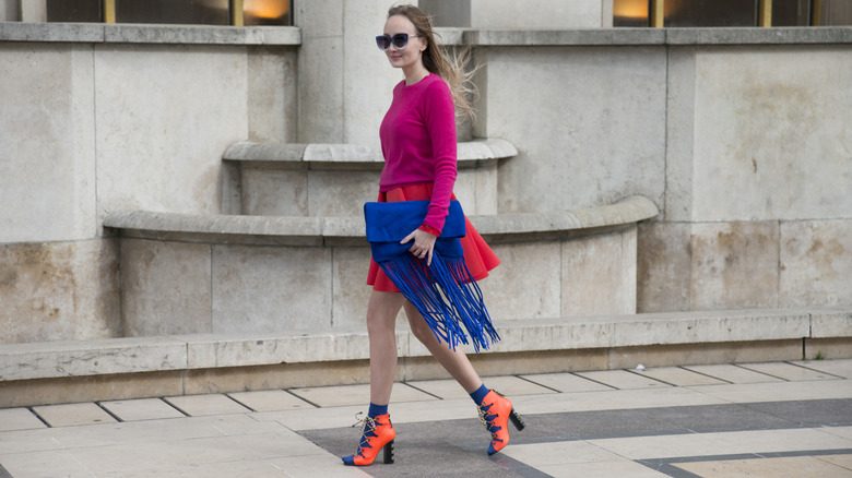 Une femme portant un pull Benetton rose avec sa jupe rouge et sa bourse bleue