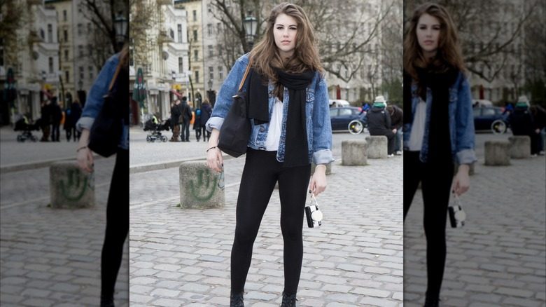 Une femme portant des leggings, des bottes, une chemise blanche et une veste en jean posant pour une photo