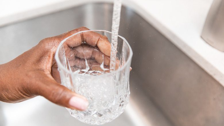 Une femme remplissant un verre d'eau d'un robinet