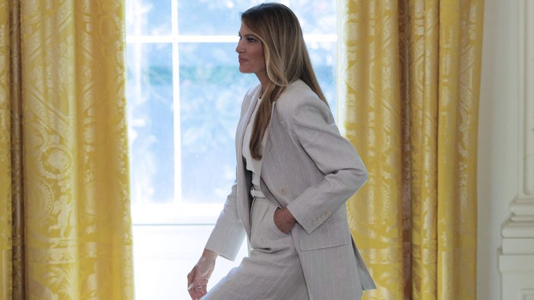 Melania Trump marchant avec une main dans son Pocker tout en portant un costume à fines rayures Max Mara
