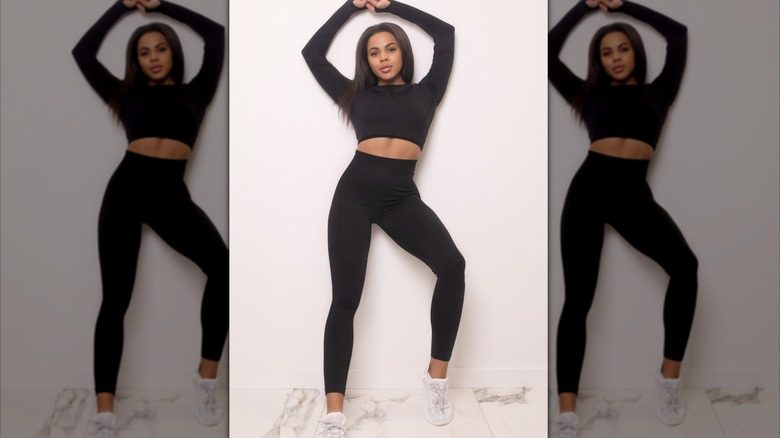 La femme pose tout en portant un crop top noir et des leggings à taille haute tout en étirant