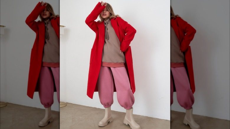 Une femme superpose un long manteau rouge sur un sweat-shirt et un pantalon de survêtement