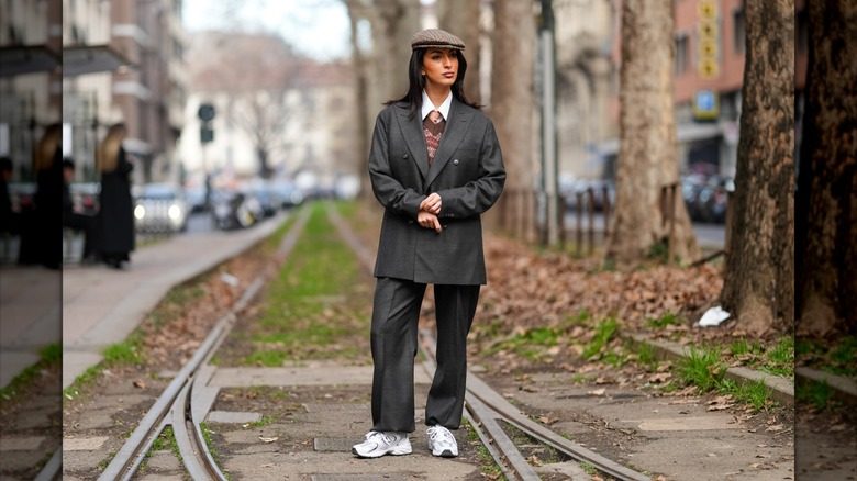Une personne porte un costume, un béret et des baskets New Balance