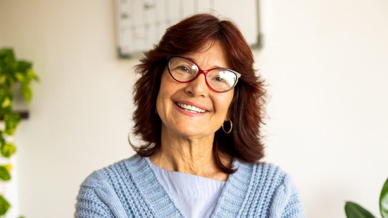 Une femme plus âgée avec un shag auburn et des lunettes sourit