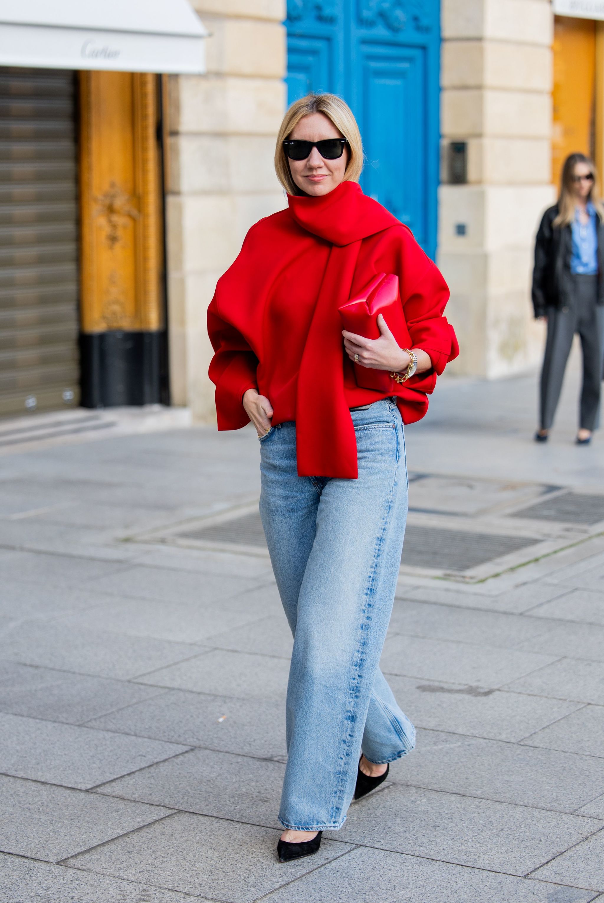 Lisa Aiken avec un look pull rouge, jean et escarpins noirs.