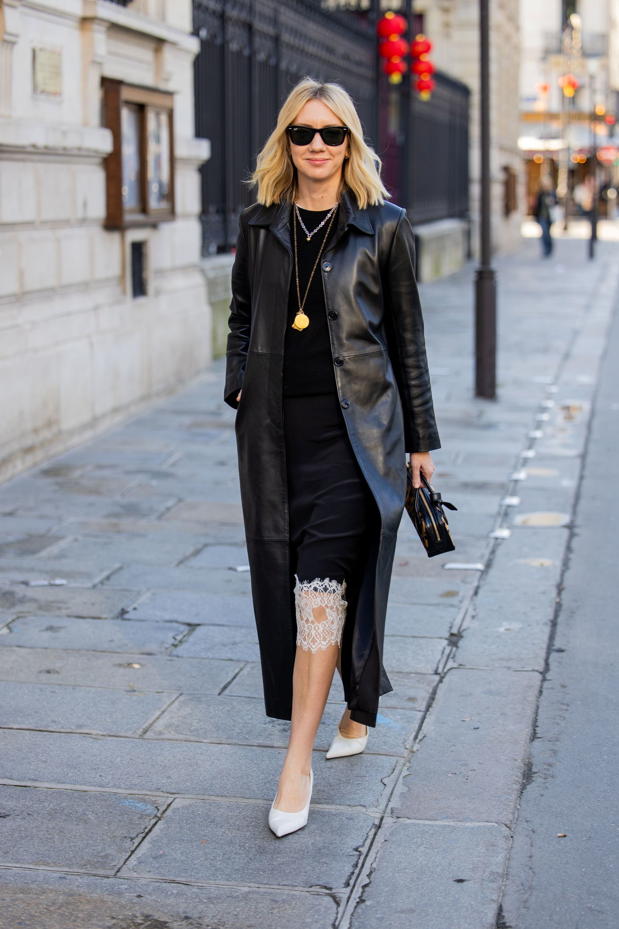 Lisa Aiken dans une robe nuisette avec ourlet en dentelle, manteau en cuir et escarpins blancs.