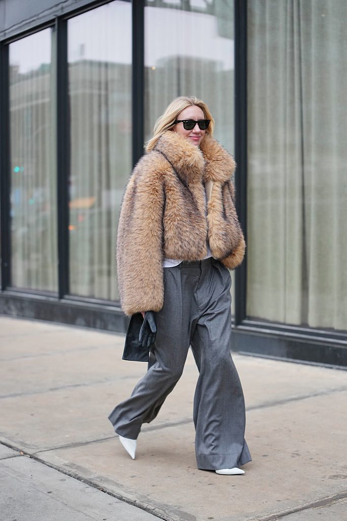 Lisa Aiken avec une veste en fourrure, un pantalon plissé gris et des escarpins blancs et la Fashion Week de New York.