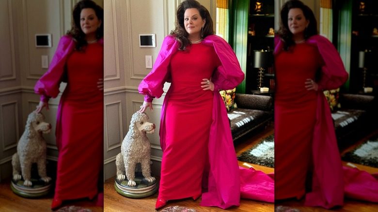 Melissa McCarthy pose en robe avec sa main sur une statue de chien à proximité