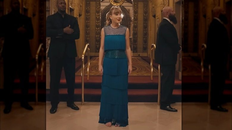 Swift dans le couloir d'un grand hôtel. Elle porte une robe bleue avec plusieurs épaisseurs de franges. Ses cheveux sont de retour en queue de cheval.