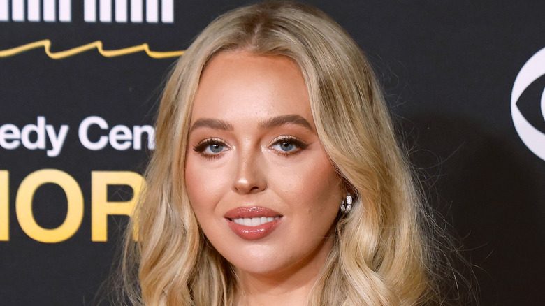 Tiffany Trump portant un brillant à lèvres pêche posant devant un fond noir