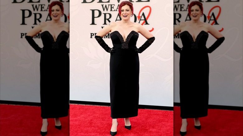 Rachel Bloom à la première de DWP2. C'est une femme à la peau claire, aux cheveux teints en rouge et à la silhouette plus ample. Elle porte une robe noire sans bretelles avec un décolleté plongeant et des gants d'opéra noirs transparents.