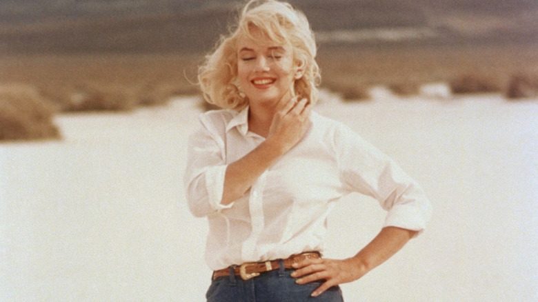 Marilyn Monroe debout sur la plage avec un jean et un haut boutonné blanc
