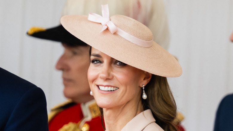 Kate Middleton sourit en portant un chapeau de soleil et des boucles d'oreilles en perles