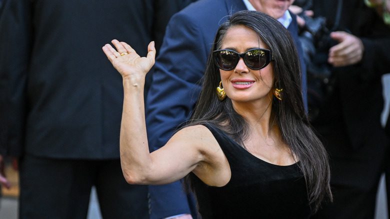 Salma Hayek saluant avec ses vêtements gris et ses lunettes de soleil