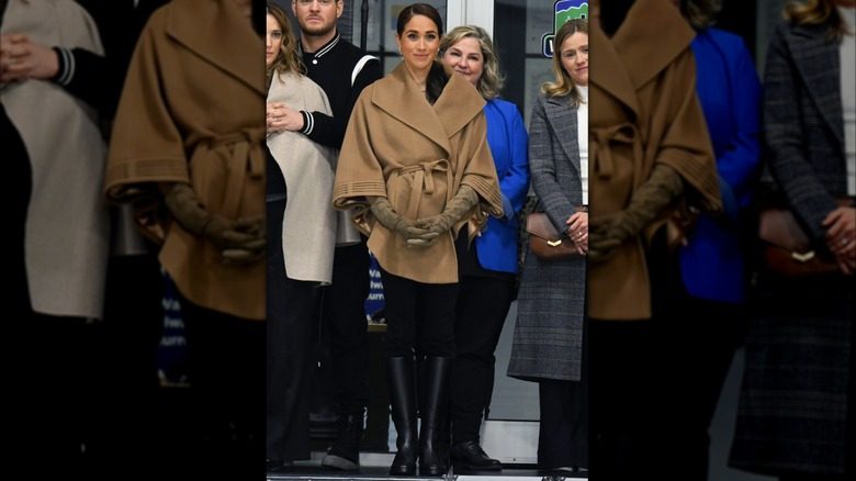 Meghan Markle portant une cape marron clair avec un pantalon de tailleur noir et de hautes bottes d'équitation en cuir lors de l'événement Invictus One Year to Go.