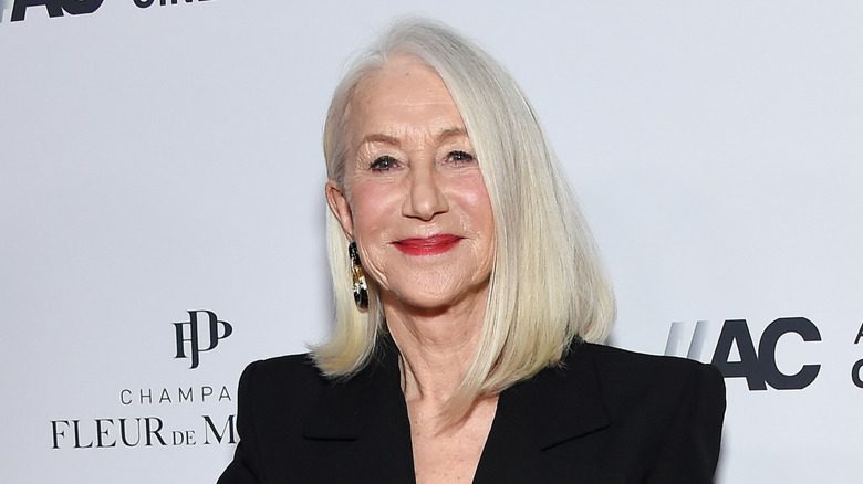 L'acteur Helen Mirren sourit avec un blazer noir et un rouge à lèvres lors d'un événement.