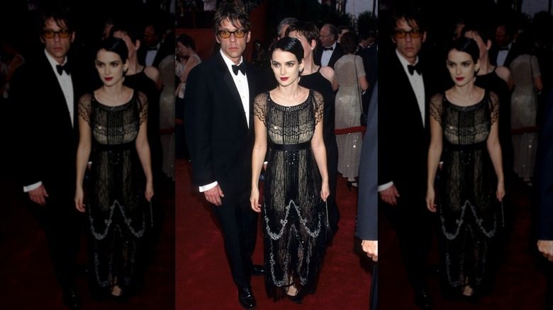 Winona Ryder posant sur un tapis rouge, vêtue d'une robe noire ornée et de cheveux lissés.