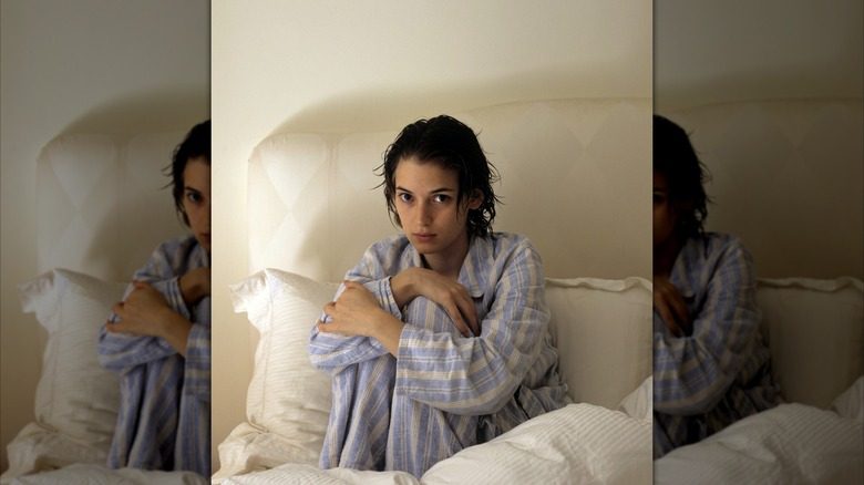 Winona Ryder posant sur son lit en pyjama à rayures bleues et cheveux mouillés.