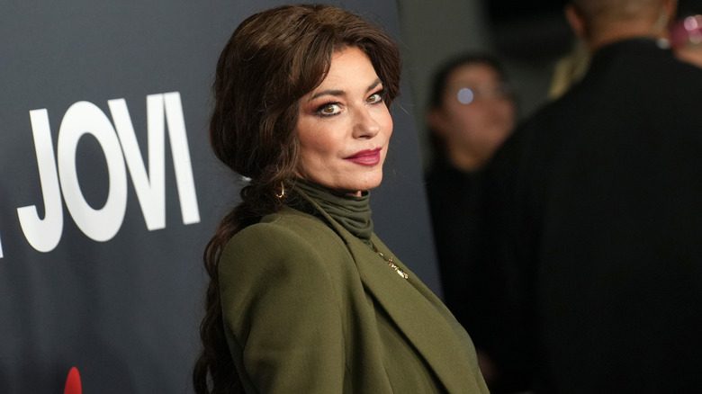 Shania Twain porte un col roulé vert olive et un blazer assorti avec des cheveux brun foncé tressés.