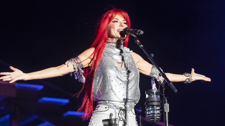 Shania Twain se produit sur scène en portant une perruque rouge vif et un haut dos nu argenté métallisé.