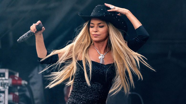 Les longs cheveux blonds de Shania Twain soufflent au vent alors qu'elle se produit sur scène avec un chapeau de cowboy noir.