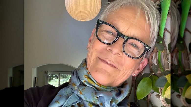 Jamie Lee Curtis penche la tête sur le côté tout en portant des lunettes et un foulard bleu dans un selfie.