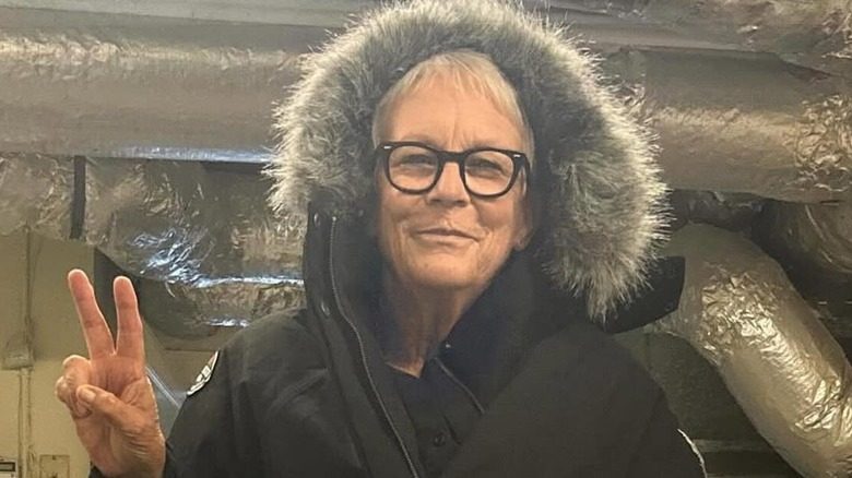 Jamie Lee Curtis fait un signe de paix tout en portant un manteau à capuche bordé de fourrure.