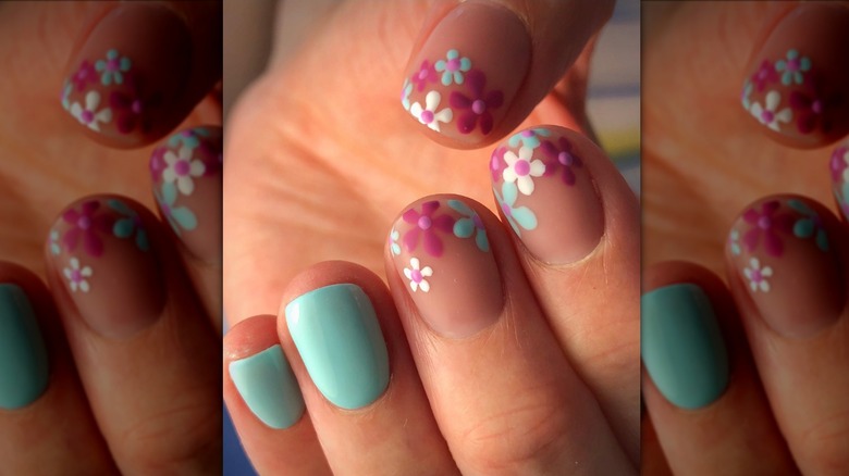 Image rapprochée d'une manucure avec deux ongles bleu clair et trois ongles avec des fleurs roses et bleues.