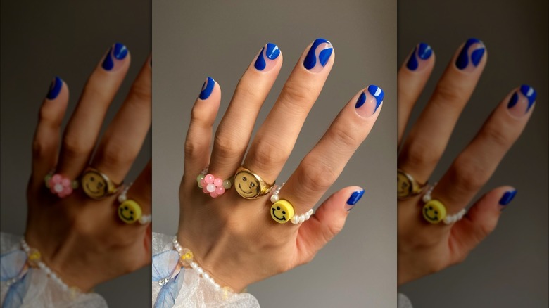 Gros plan d'une manucure bleue ondulée sur une main avec plusieurs anneaux de style années 60.