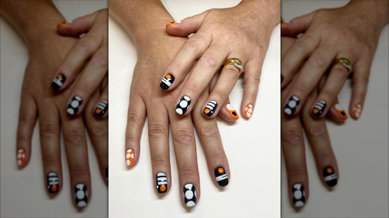 Regardez de près une manucure de style Mod avec des formes géométriques noires, blanches et orange.