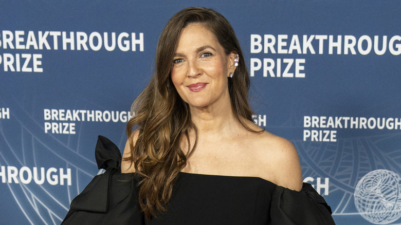 Drew Barrymore posant sur un tapis rouge vêtue d'une robe bustier noire.