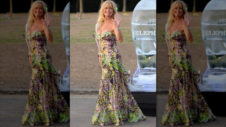 Goldie Hawn saluant dehors, vêtue d'une robe fluide et colorée.