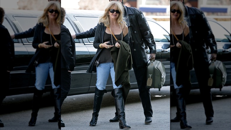 Goldie Hawn photographiée près d'une voiture dans une rue portant un jean, des bottes noires, un haut noir et des lunettes de soleil.