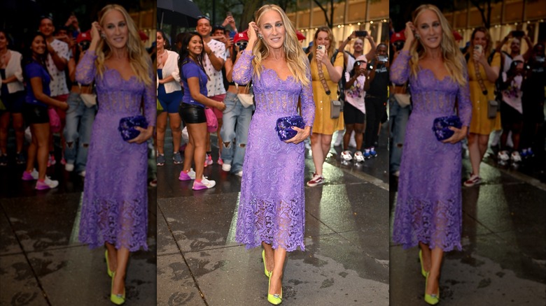 Sarah Jessica Parker posant lors d'un événement en 2023, la main près de la tête, vêtue d'une robe en dentelle violette.