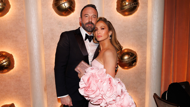Ben Affleck portant un costume et Jennifer Lopez portant une robe rose à volants posant ensemble lors d'un événement sur le tapis rouge.