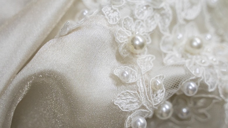 Une image en gros plan d’une robe de mariée avec de la dentelle et des perles.