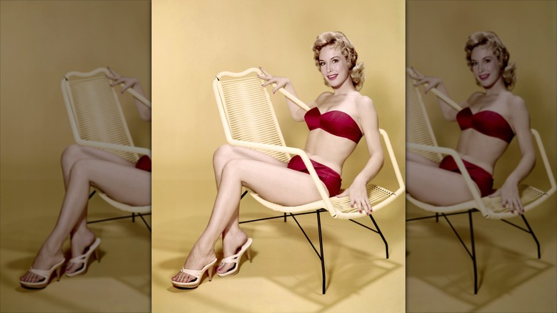 Barbara Eden est assise sur une chaise et porte un bikini rouge et des talons blancs.