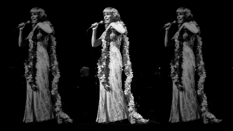 Barbara Eden tient un micro et porte une robe ornée d'or et un boa en plumes.