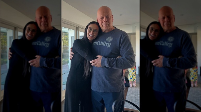 Demi Moore porte des lunettes et une tenue noire serrant Bruce Willis vêtu d'un sweat-shirt bleu.