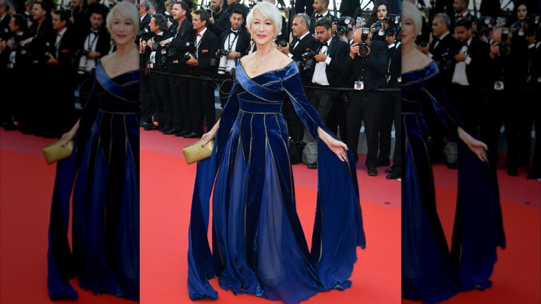 Helen Mirren posant sur le tapis rouge en 2018, vêtue d'une robe royale en velours bleu à manches longues fluides.