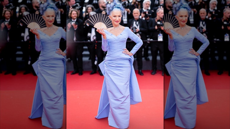 Helen Mirren tenant un éventail sur le tapis rouge en 2023, vêtue d'une robe pervenche et de cheveux assortis.