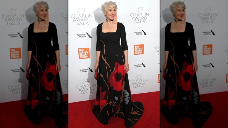 Helen Mirren posant sur le tapis rouge en 2018 vêtue d'une longue robe noire à fleurs rouges.