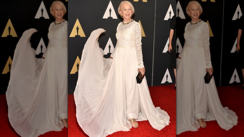 Helen Mirren souriante sur le tapis rouge en 2015, vêtue d'une robe blanche avec une jupe fluide.