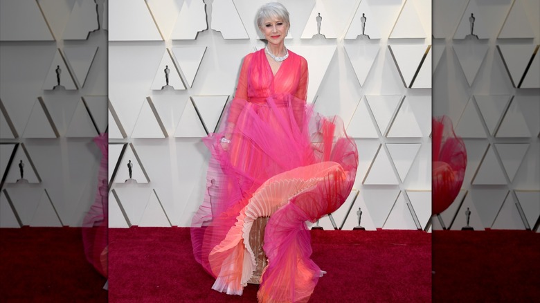Helen Mirren posant sur le tapis rouge en 2019 vêtue d'une robe rose vif avec une jupe qui flotte au vent.