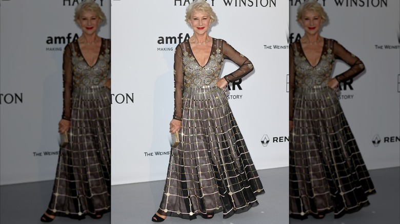 Helen Mirren posant avec sa main sur sa hanche lors d'un événement en 2016, vêtue d'une robe noire et argentée détaillée.