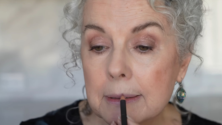 Femme plus âgée aux cheveux gris bouclés appliquant un crayon à lèvres